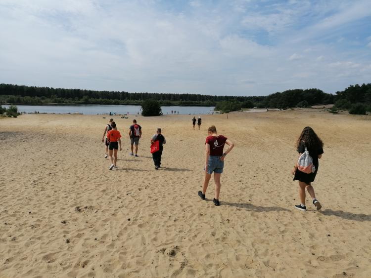 groepje jongeren die verspreid over zandvlakte wandelt met op de achtergrond bossen